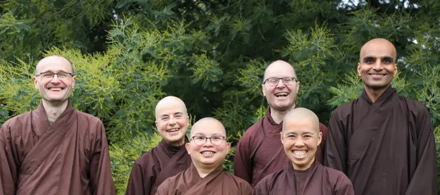 6 monks standing Infront of greenery smiling at the camera