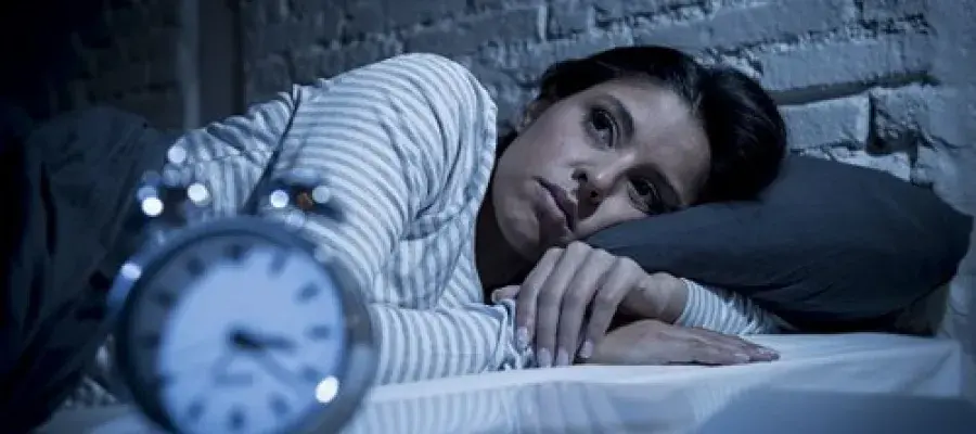 Photograph of a woman lying awake in bed staring at a clock. 