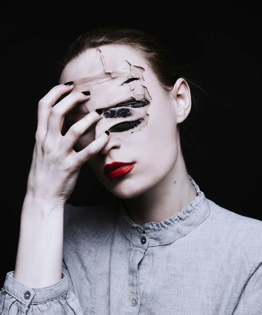 Image of a woman in a grey shirt pulling her hand across her face. The image shows her hand pulling parts of her face in pain.