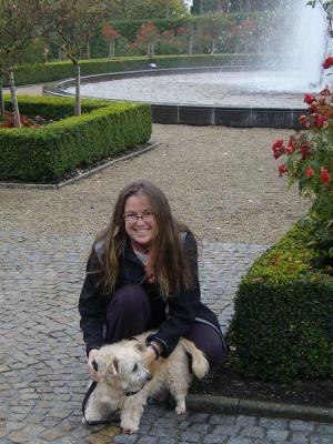 Photograph of Associate Chaplain Urzula Glienecke crouched down patting a dog. Urzula is in a garden with a fountain behind her.