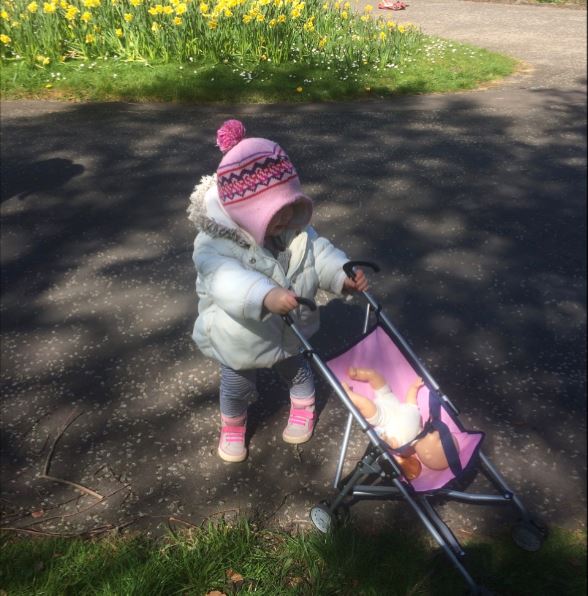 Image of little girl pushing a toy pram in the park