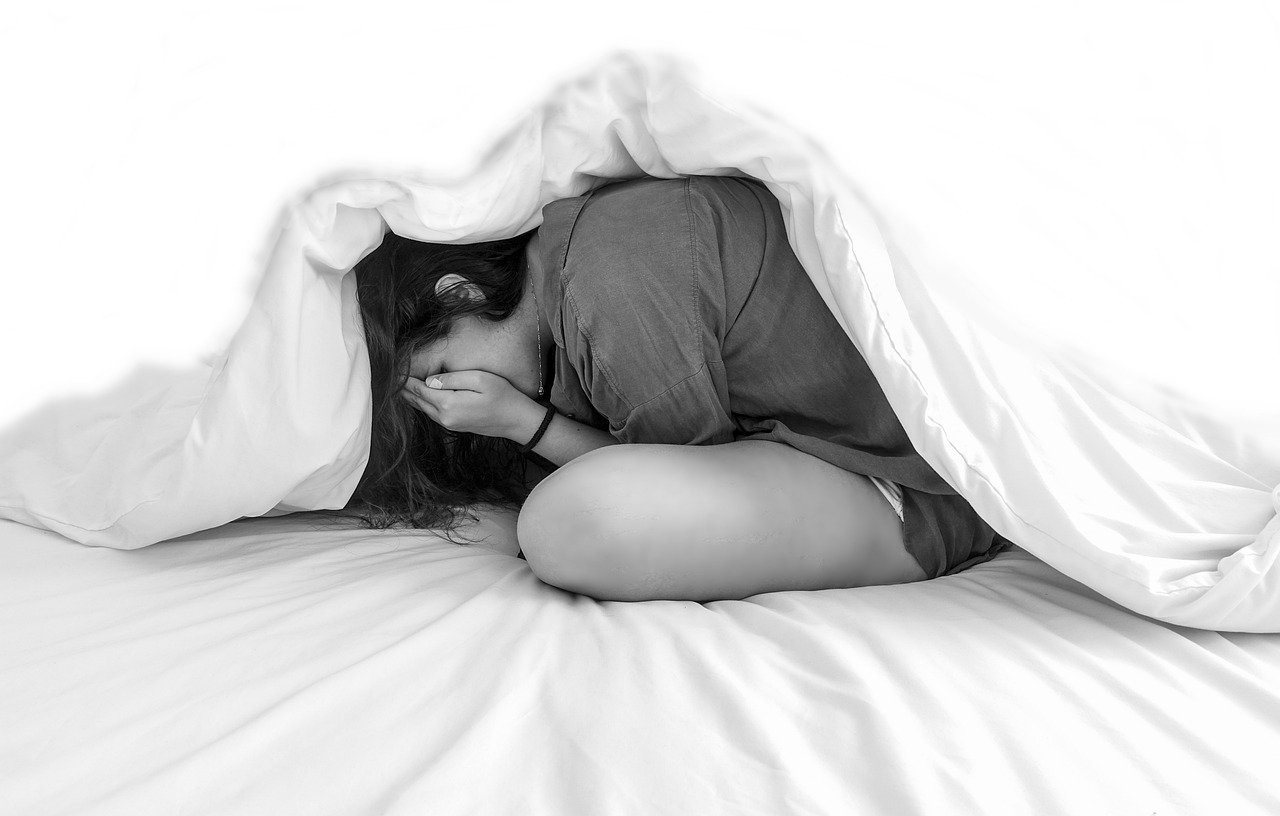 A black and white photo of a woman hiding underneath a duvet.