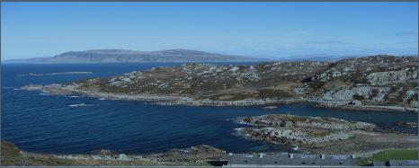 Photograph of the Island of Mull. There is landscape with blue skies, hills in the background and sea meeting the land.