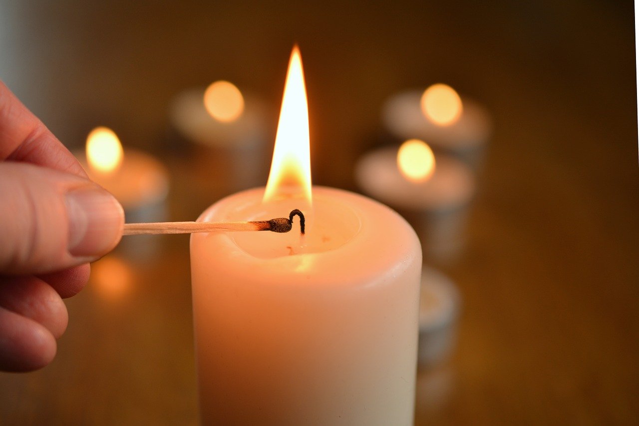 Photograph of a white candle being lit by a match. 