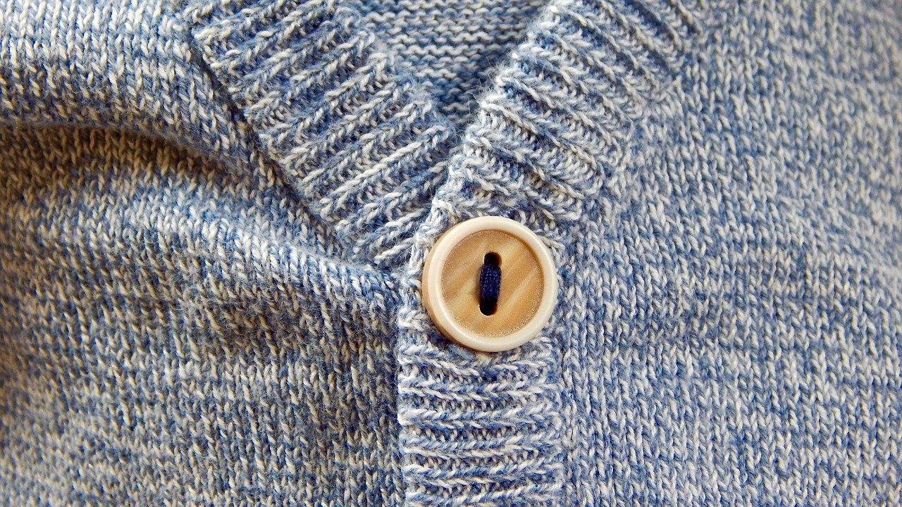 A close up photograph of a blue cardigan with a brown button.