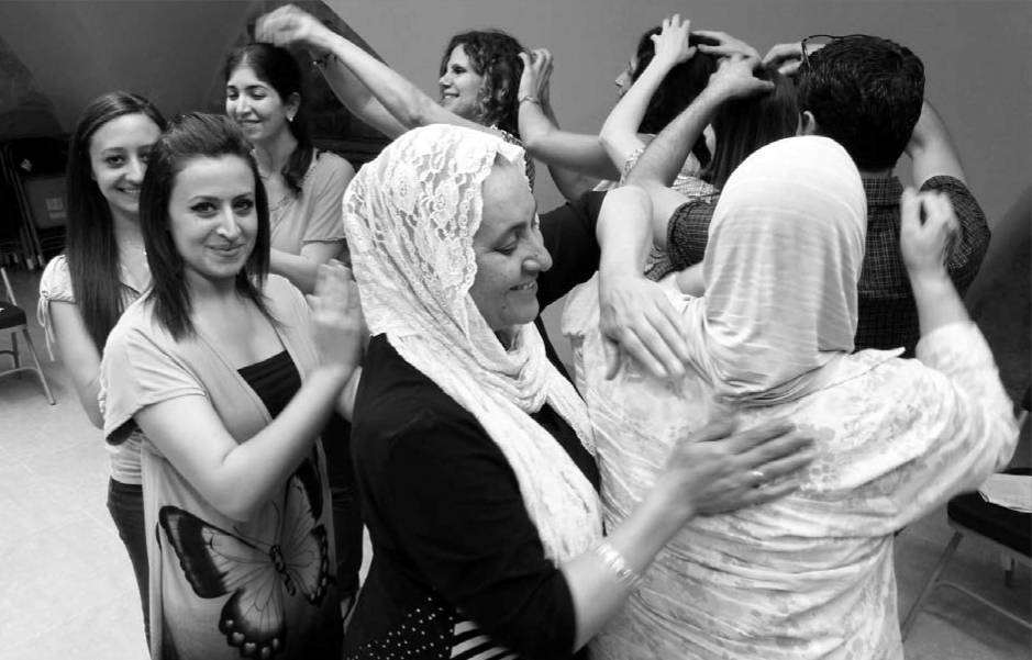 Photograph of a group of women doing a drum massage - they are all stood in a group with their hands on the shoulders of the person in front of them. 