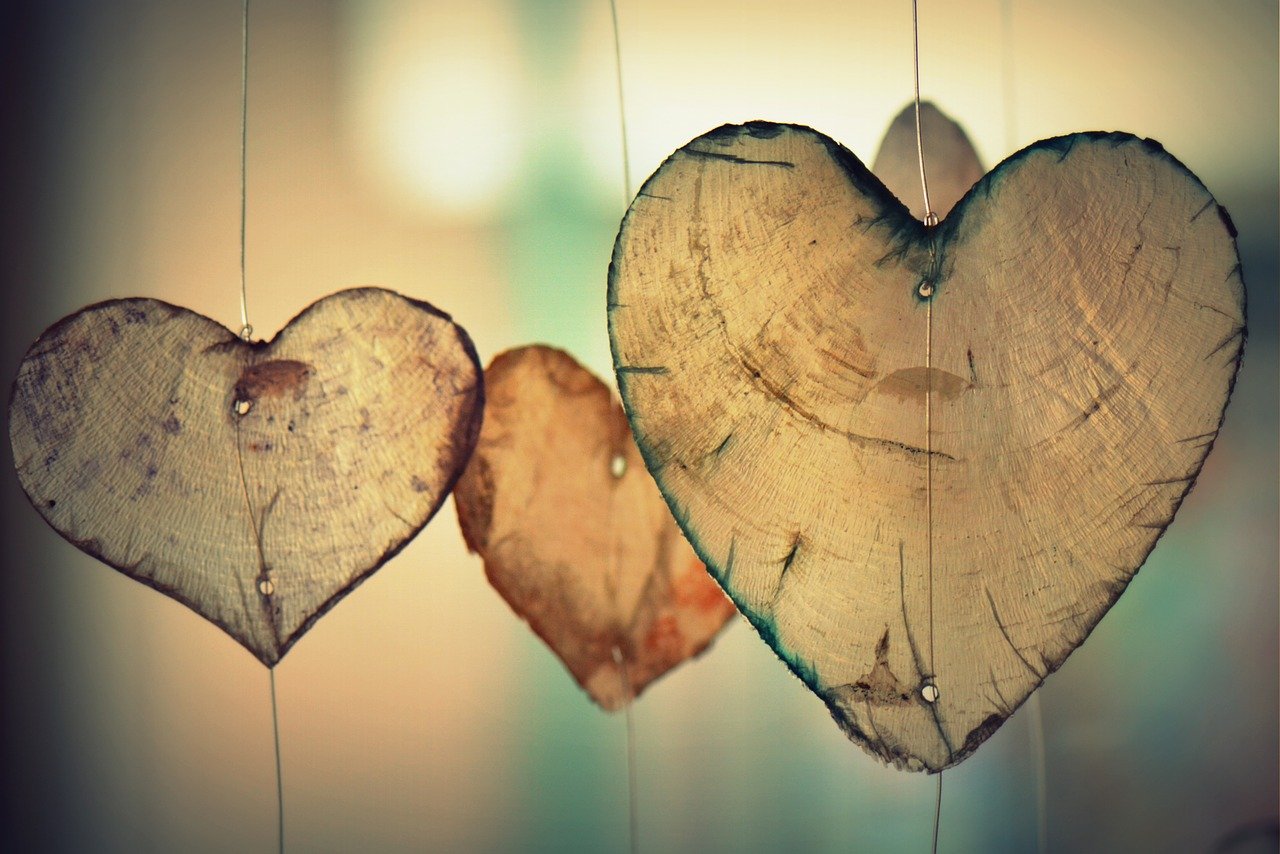 A photograph of 3 wooden decorations in the shape of love hearts. 