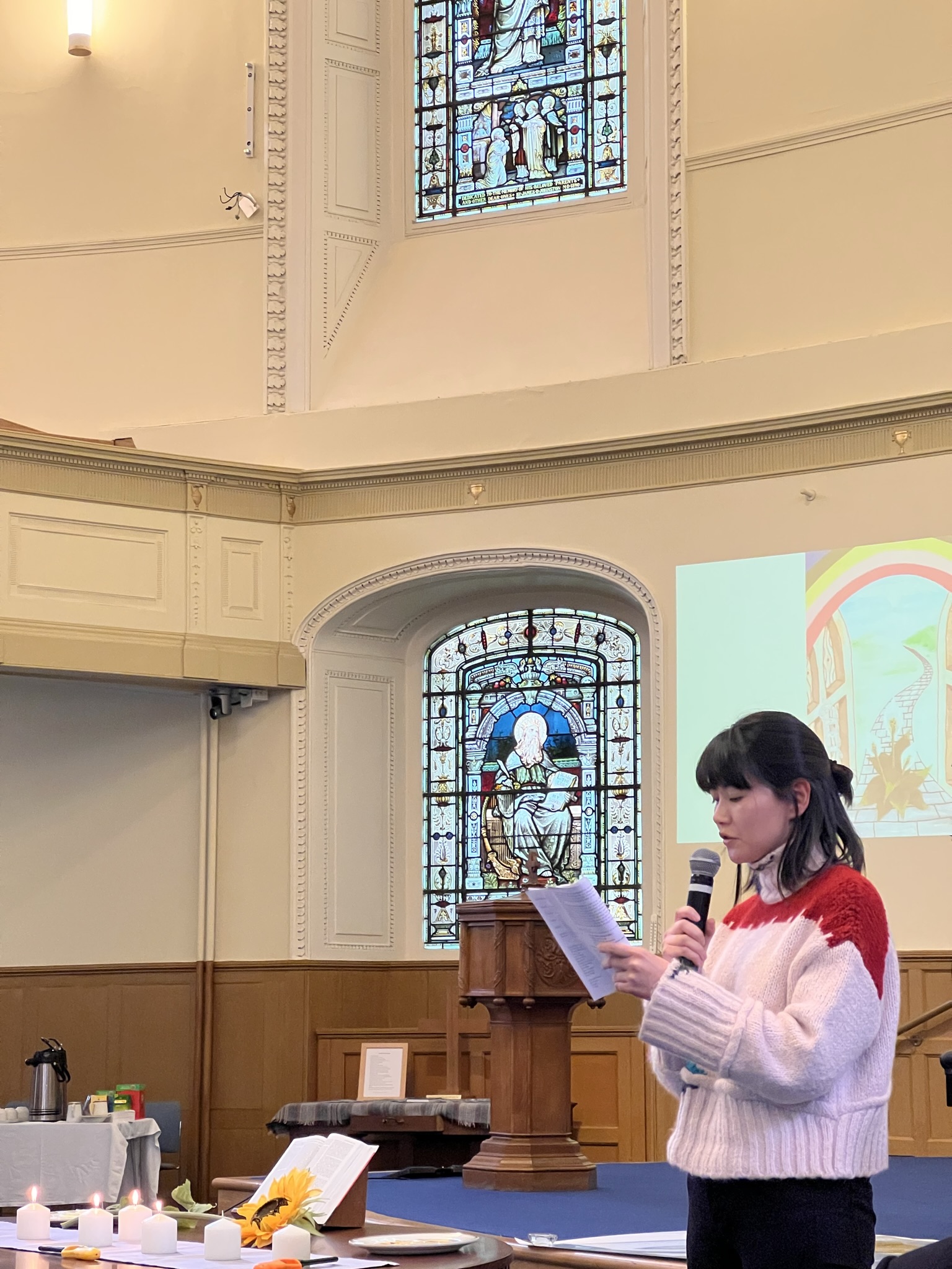 Photograph of inside a church of World Day of Prayer. A student is standing at the front of a church reading to those in attendance