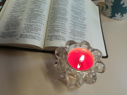 Image of a book open, with a lit candle beside it. 