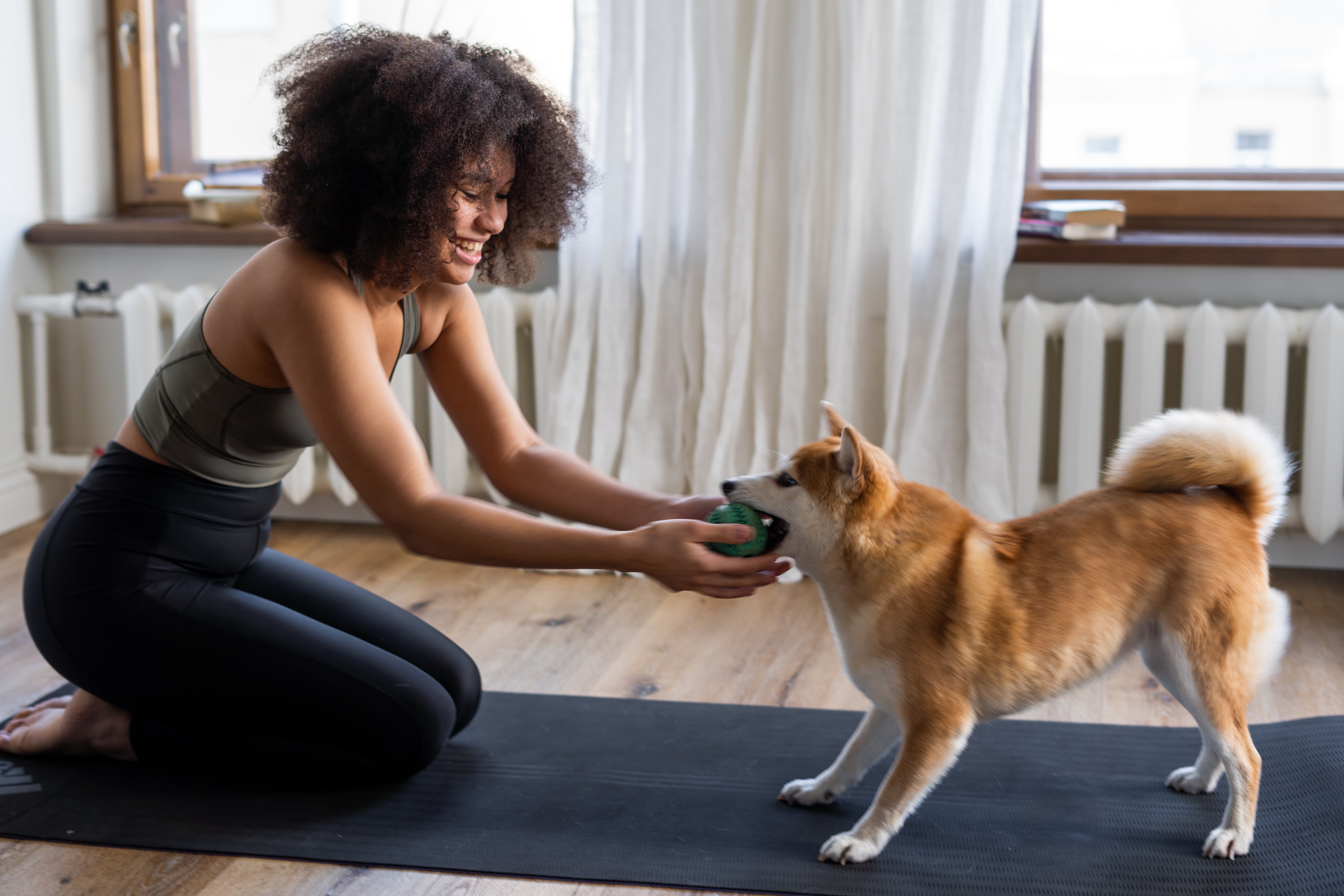 A woman sitting on a yoga mat playing with her dog