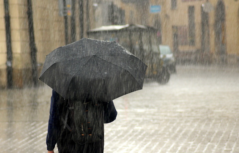 A photo of somebody holding an umbrella up while it pours down with rain in a city.