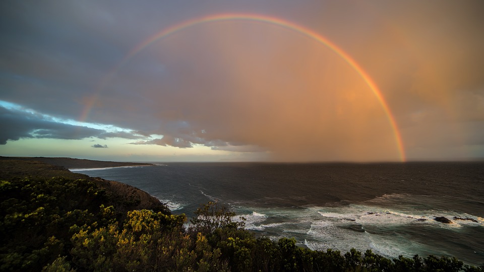 a photo of a rainbow stretching from the sea to the land 