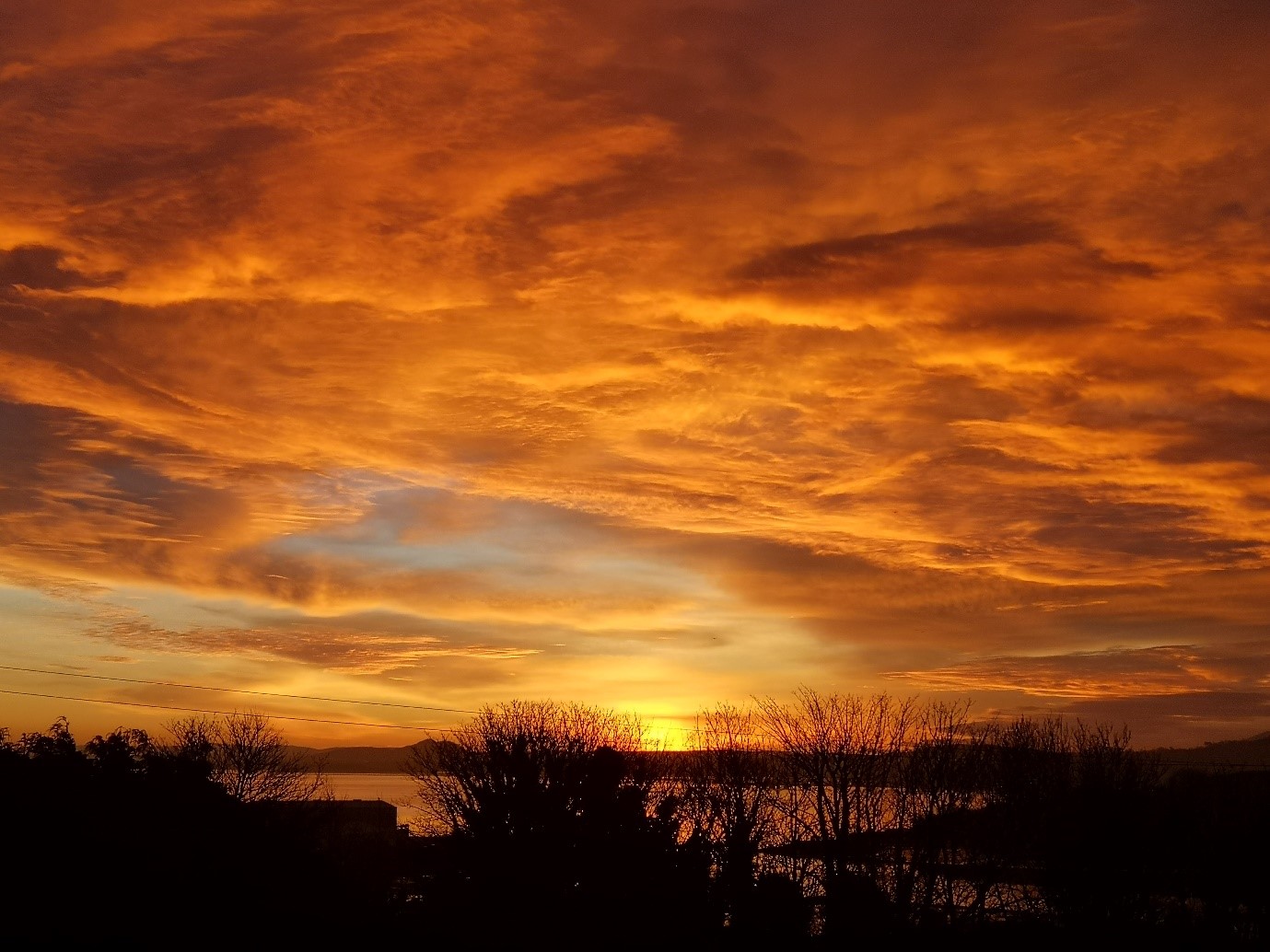 Photograph of a sunset, the sky above is a mix of red,orange and yellow. 